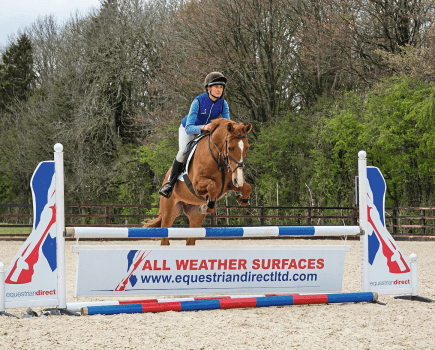 Pictured is a horse and rider jumping a showjump on an Equestrian Direct all-weather surface
