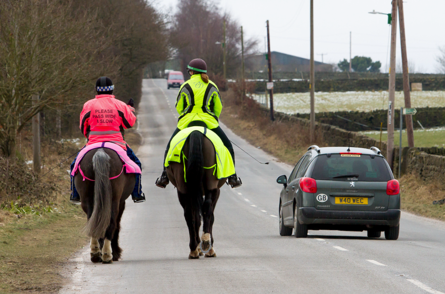 Pictured are two horse riders wearing high vis for safety while hacking along a main road