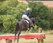 A rider is pictured wearing a black body protector while jumping a cross-country jump on a dark horse