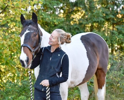 Pictured is a coloured horse being led by a lady who is stroking the horse's head; their body language is relaxed and happy