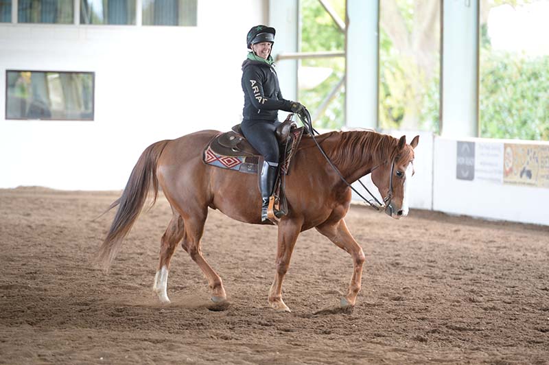 Pictured is a female riding a chestnut horse Western style