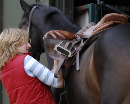 Pictured is a rider doing up their horse's girth, an essential item of tack