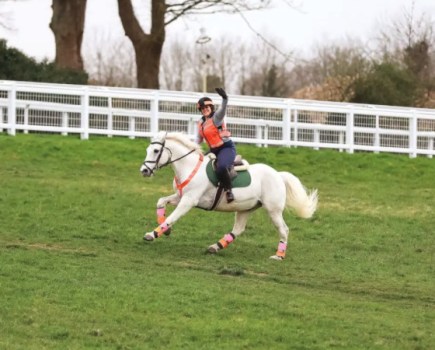 Pictured is a rider smiling while hacking a horse at canter. Trail riding does wonders for horse and rider's mental and physical health