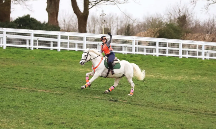 Pictured is a rider smiling while hacking a horse at canter. Trail riding does wonders for horse and rider's mental and physical health