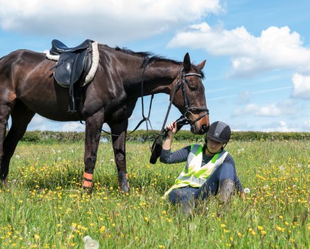 Pictured is a horse rider on the floor after falling off, with her horse stood next to her; brain injuries in horse riders are frequent